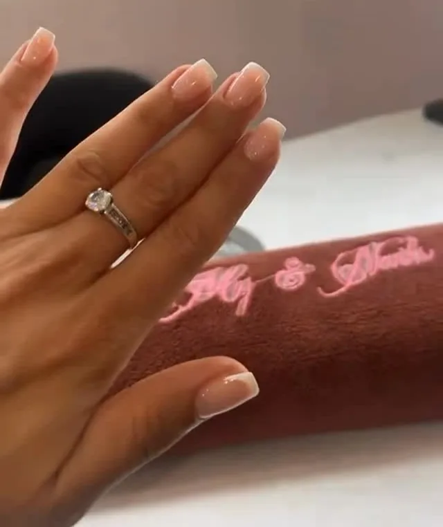 Main posée sur l’accoudoir brodé du salon, ongles ballerine en french nude discrète.