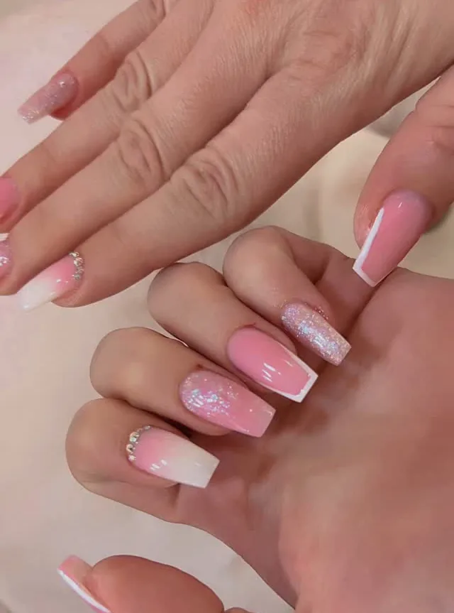 Ongles carrés en dégradé rose et blanc, un doigt pailleté, strass à la base.